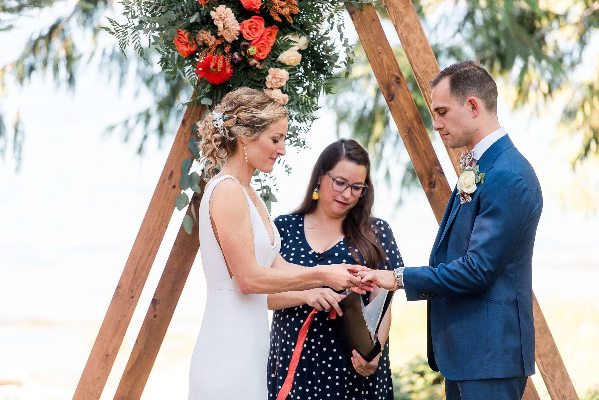 Bride and groom exchanging rings under flowers