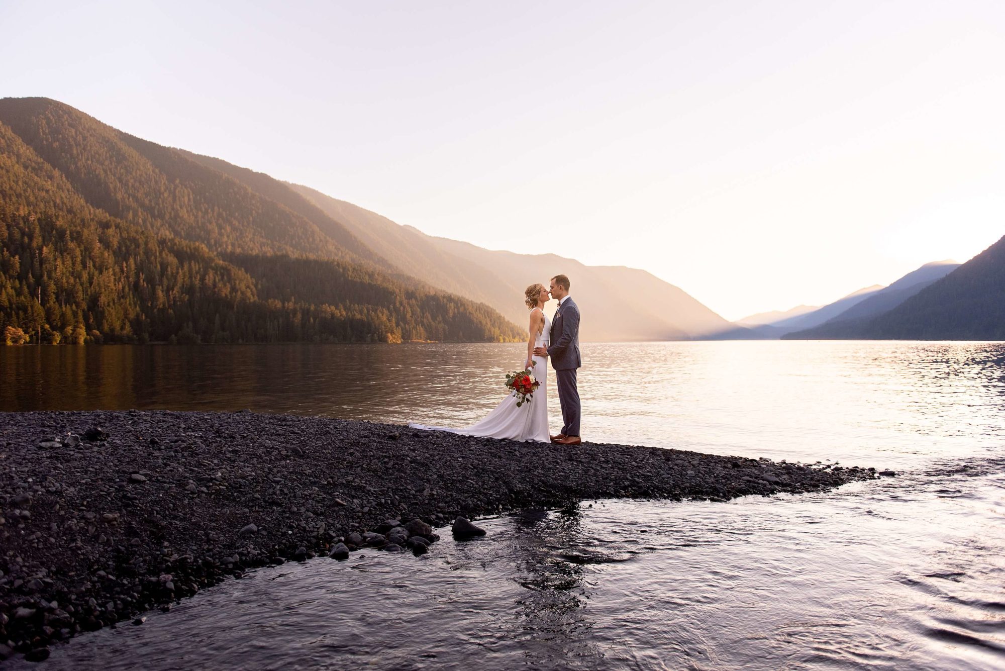 groom kissing bride by lake at NatureBridge Wedding venue
