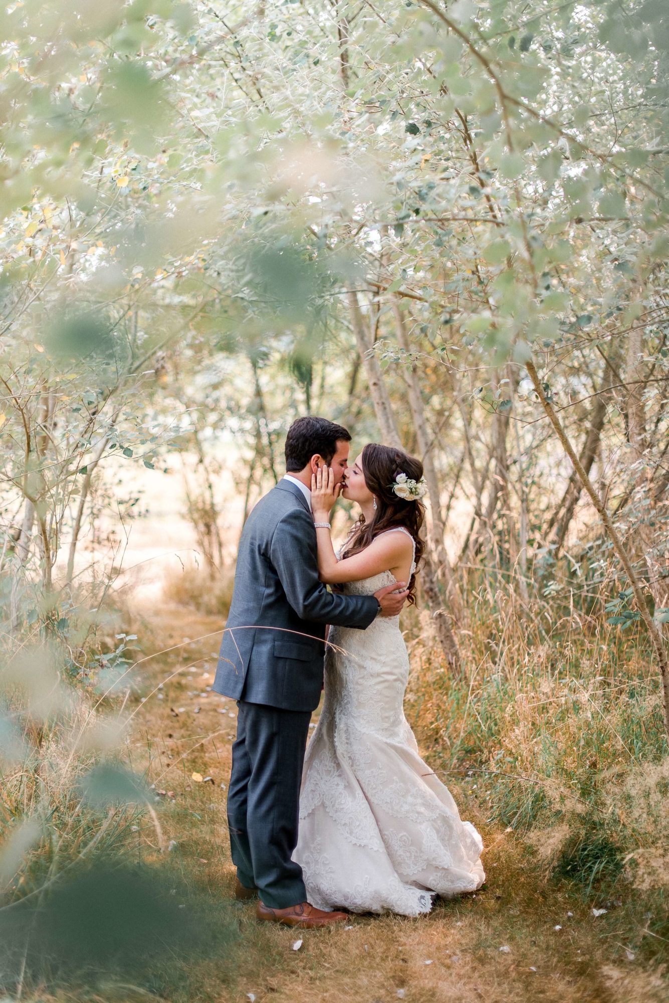 bride and groom kiss in small tree lined path at fireseed catering wedding venue