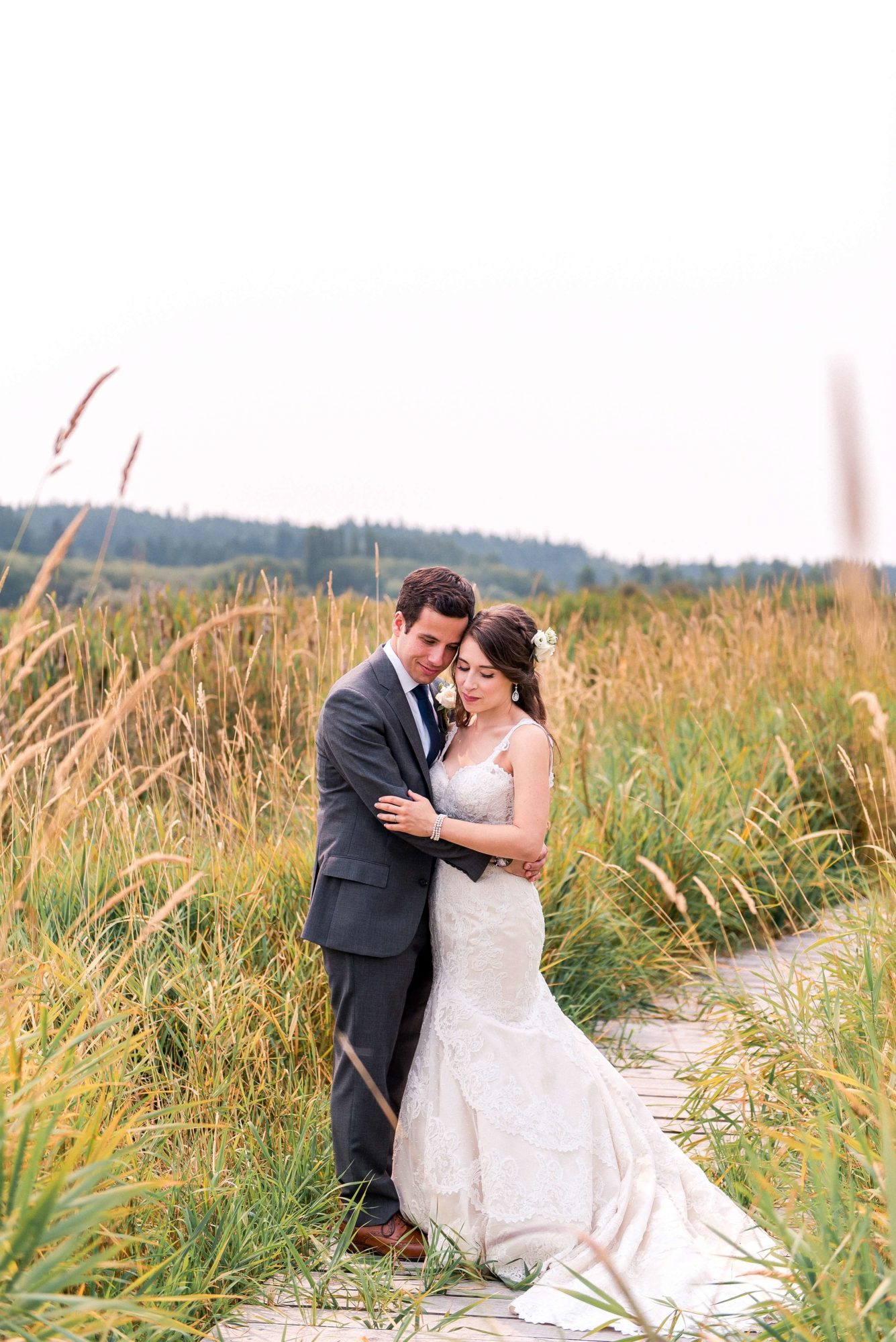 tall golden grass surrounds bride and groom hugging on the boardwalk path at fireseed catering wedding venue