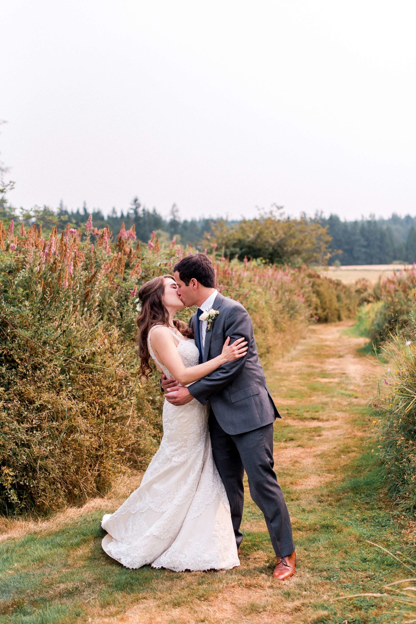 bride and groom kiss in winding grass path through flowers