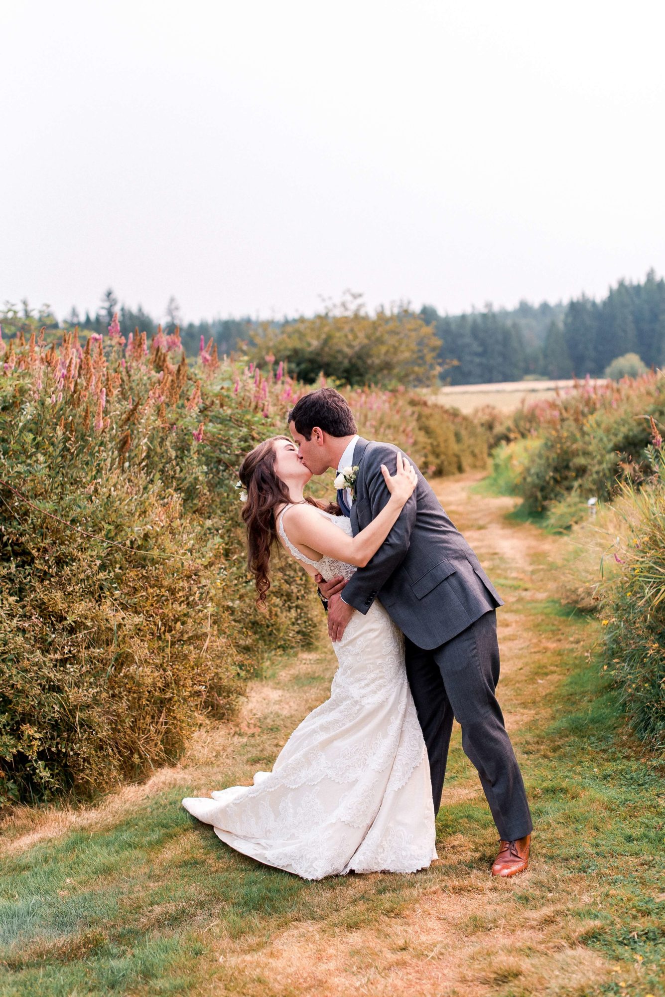 bride and groom dip and kiss in path through fields of flowers at fireseed catering wedding venue
