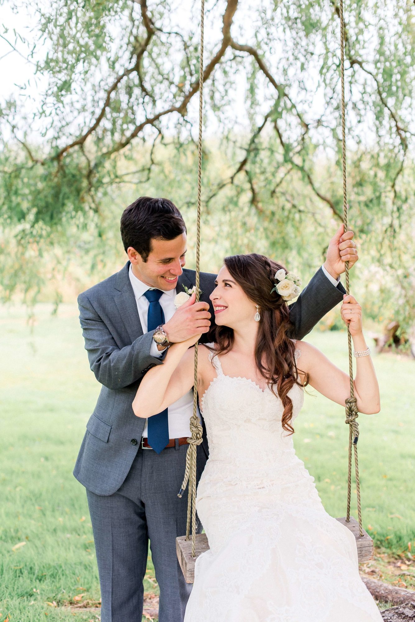 bride and groom play on a swing under the willow tree