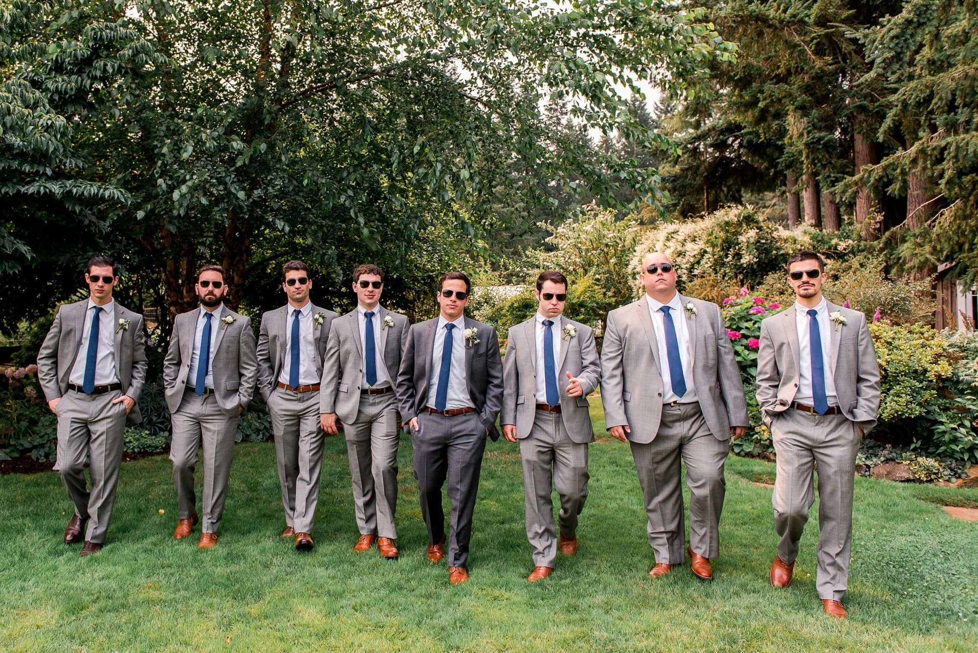 Groom and his groomsmen wearing sunglasses while walking through garden