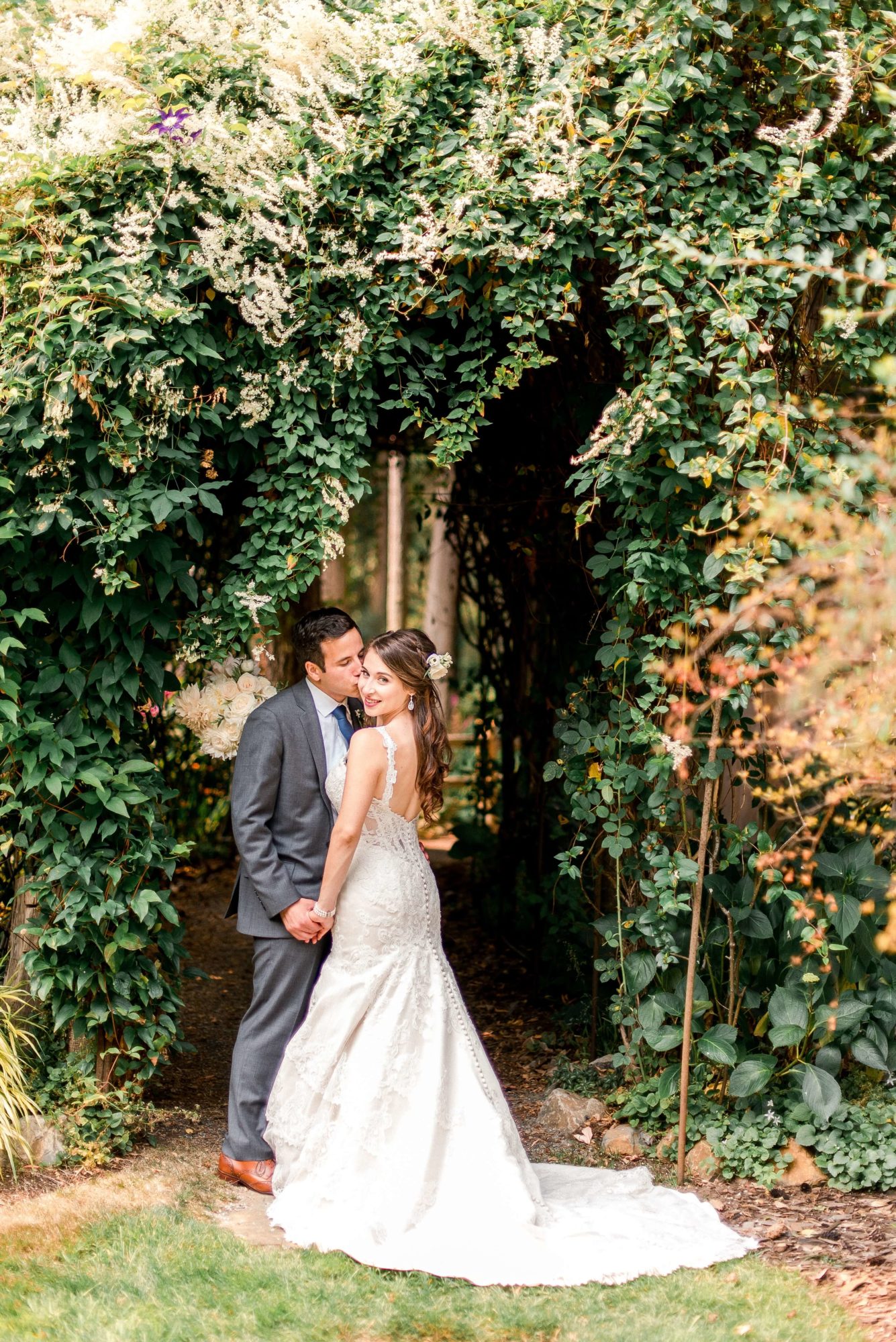 groom kissing bride's cheek under a vine arch at Fireseed catering wedding venue