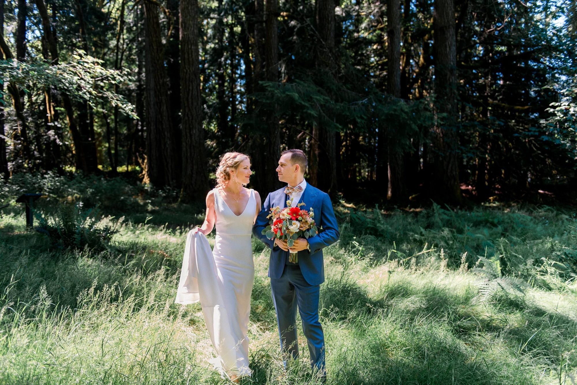 groom holding the wedding bouquet and assisting bride while walking through a field