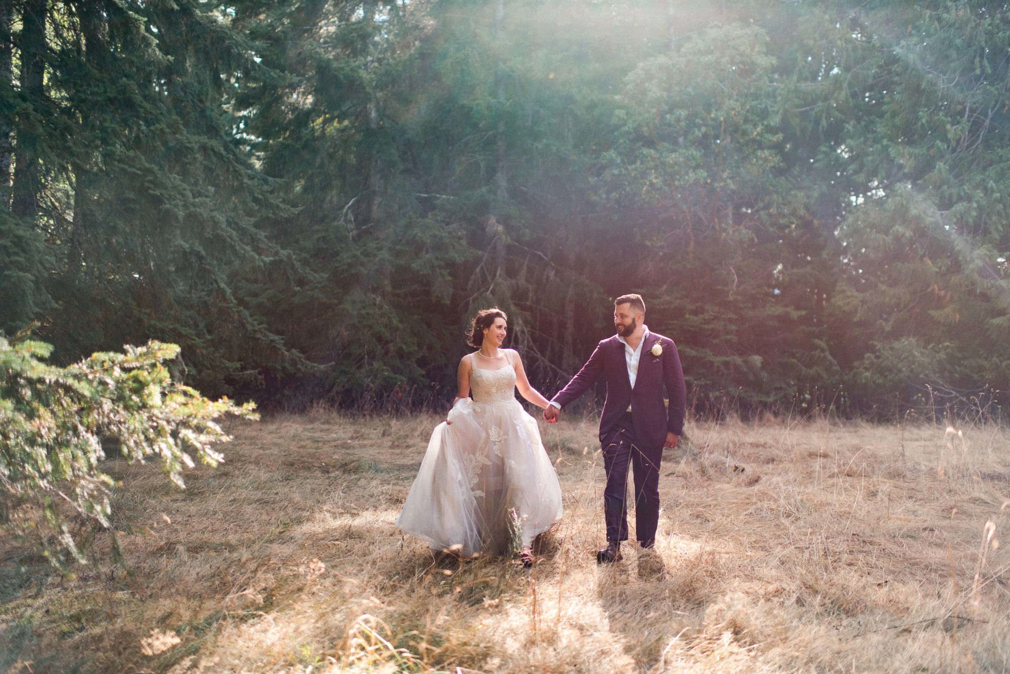 bride and groom walking through a field of golden grass hiding in the forest at The Lodge at St. Edwards
