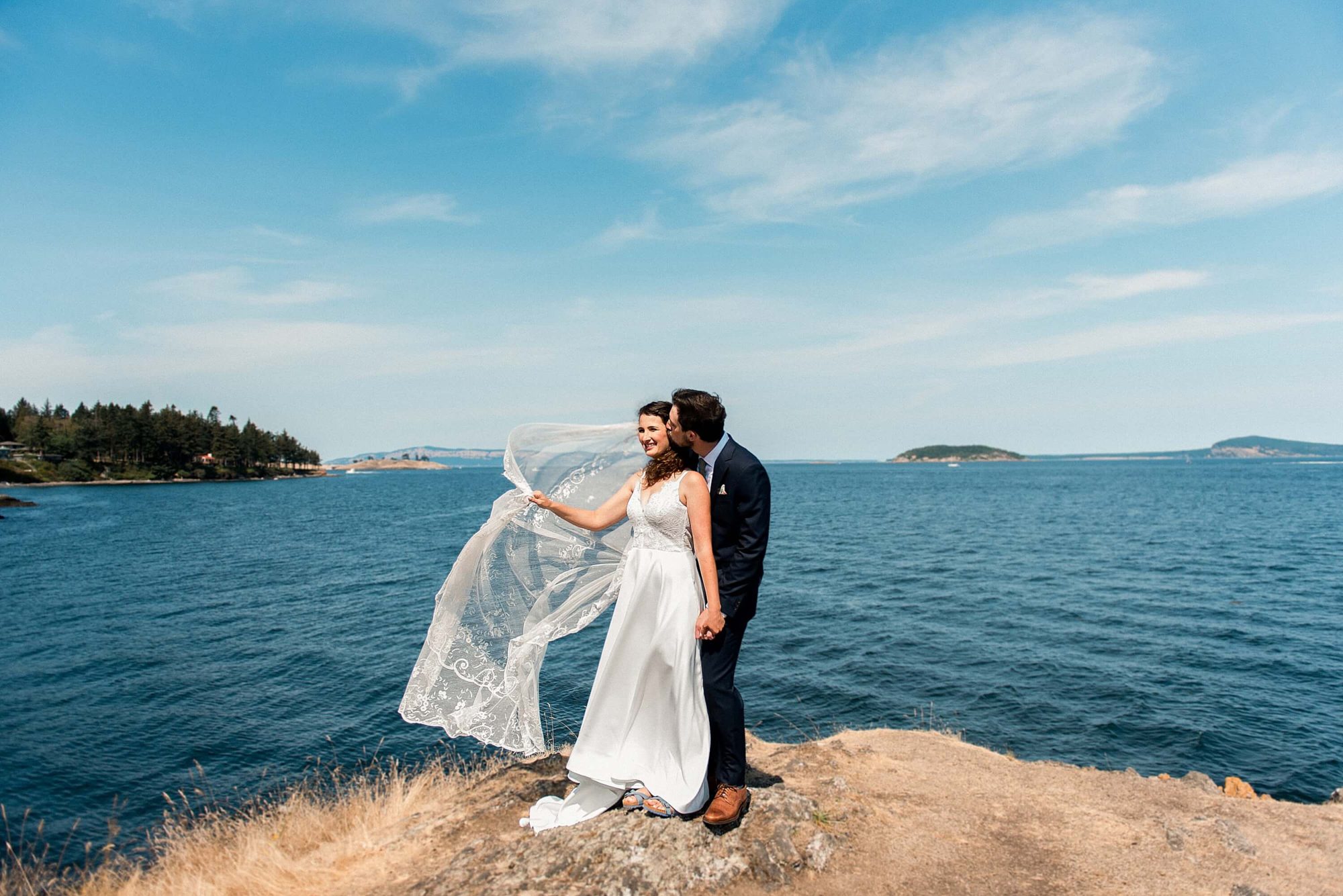 bride and groom on a rock kissing with the veil flying at their San Juan Island Wedding