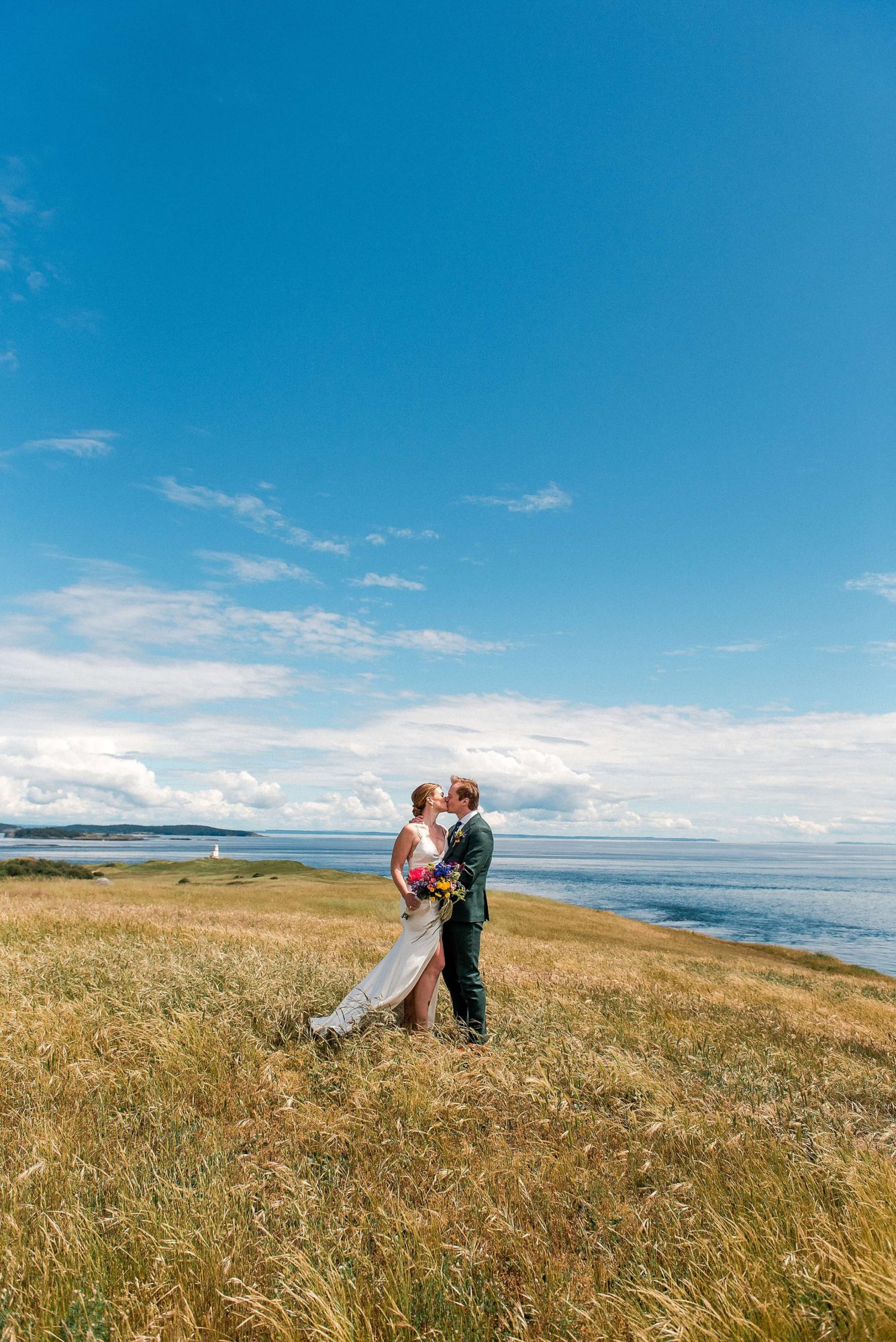 bride and groom kissing in a field near the water at their San Juan Island Wedding
