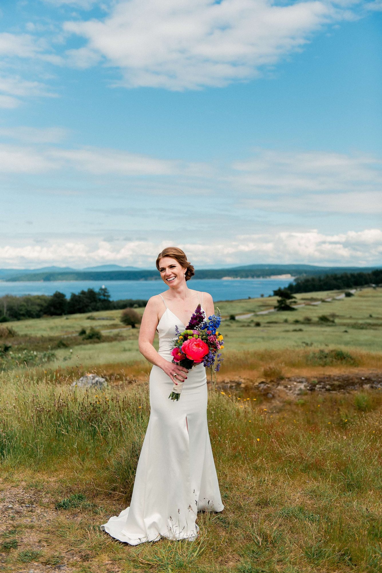 bride laughing into the distance while holding her bouquet at their San Juan Island Wedding