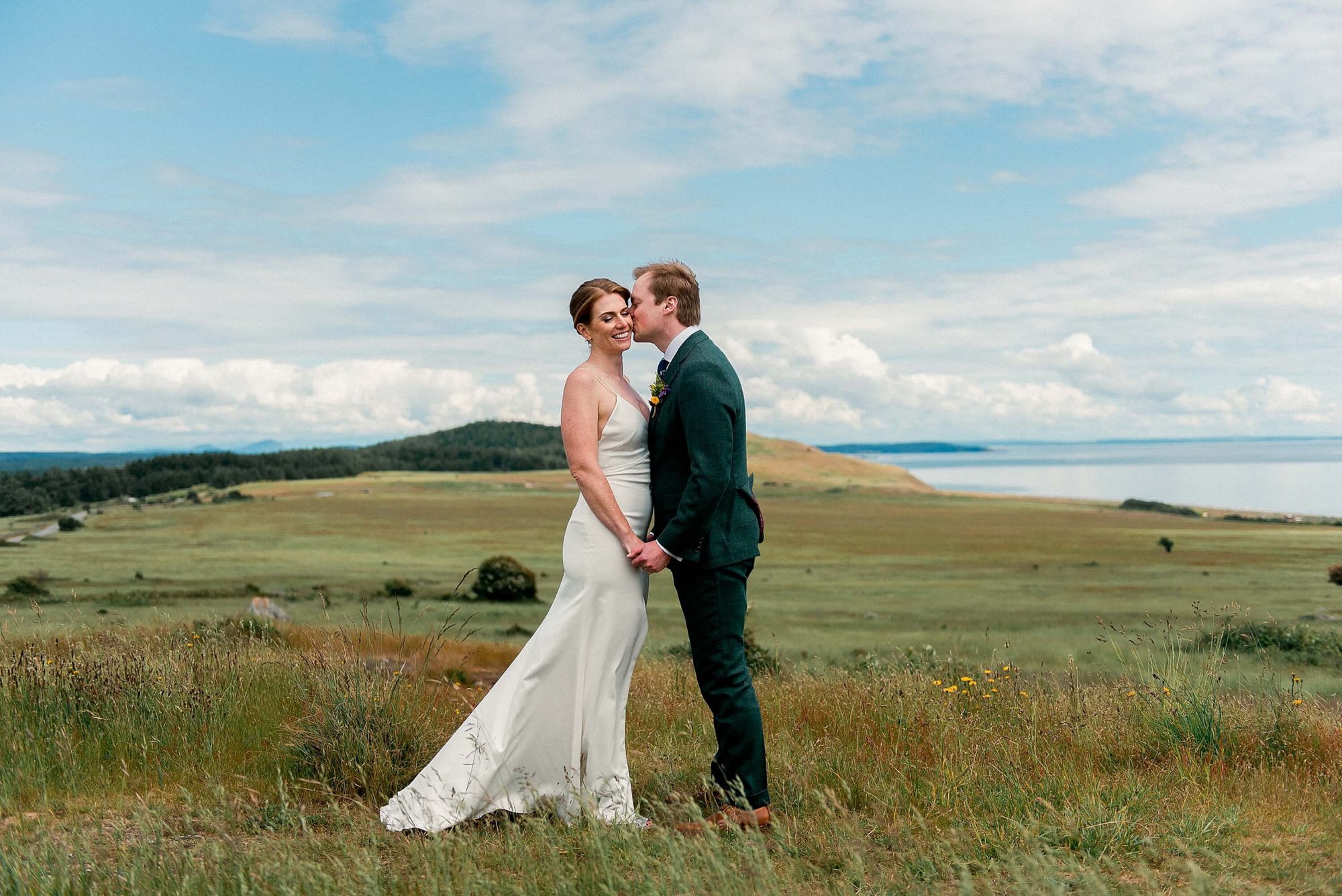 groom kissing his bride on the cheek in the rolling hills at their San Juan Island Wedding