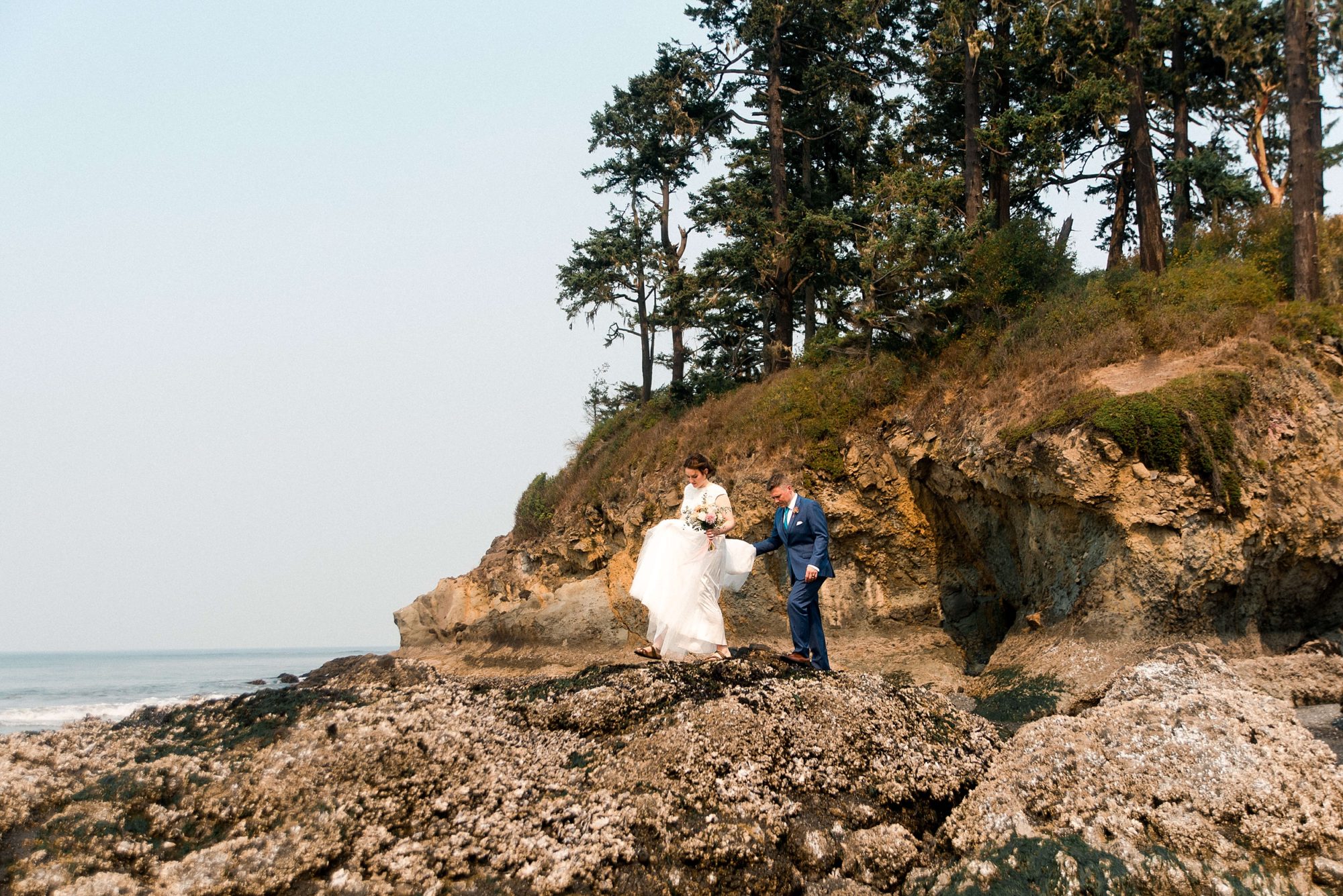 groom helping his bride onto the rock formation at their Seabrook wedding