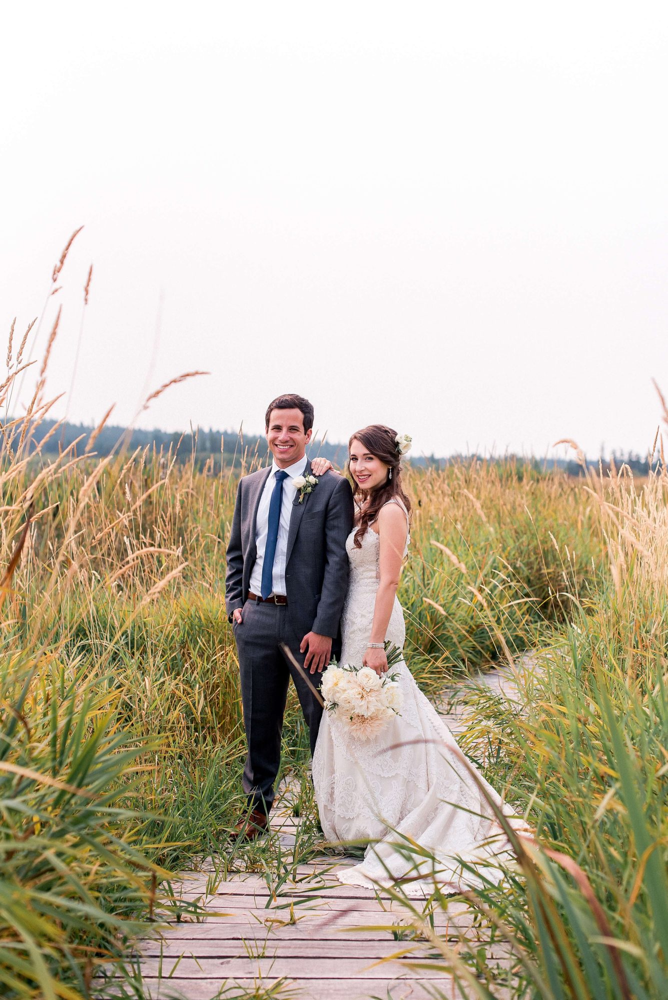 bride and groom standing on a boardwalk in a large field at their Whidbey Island Wedding