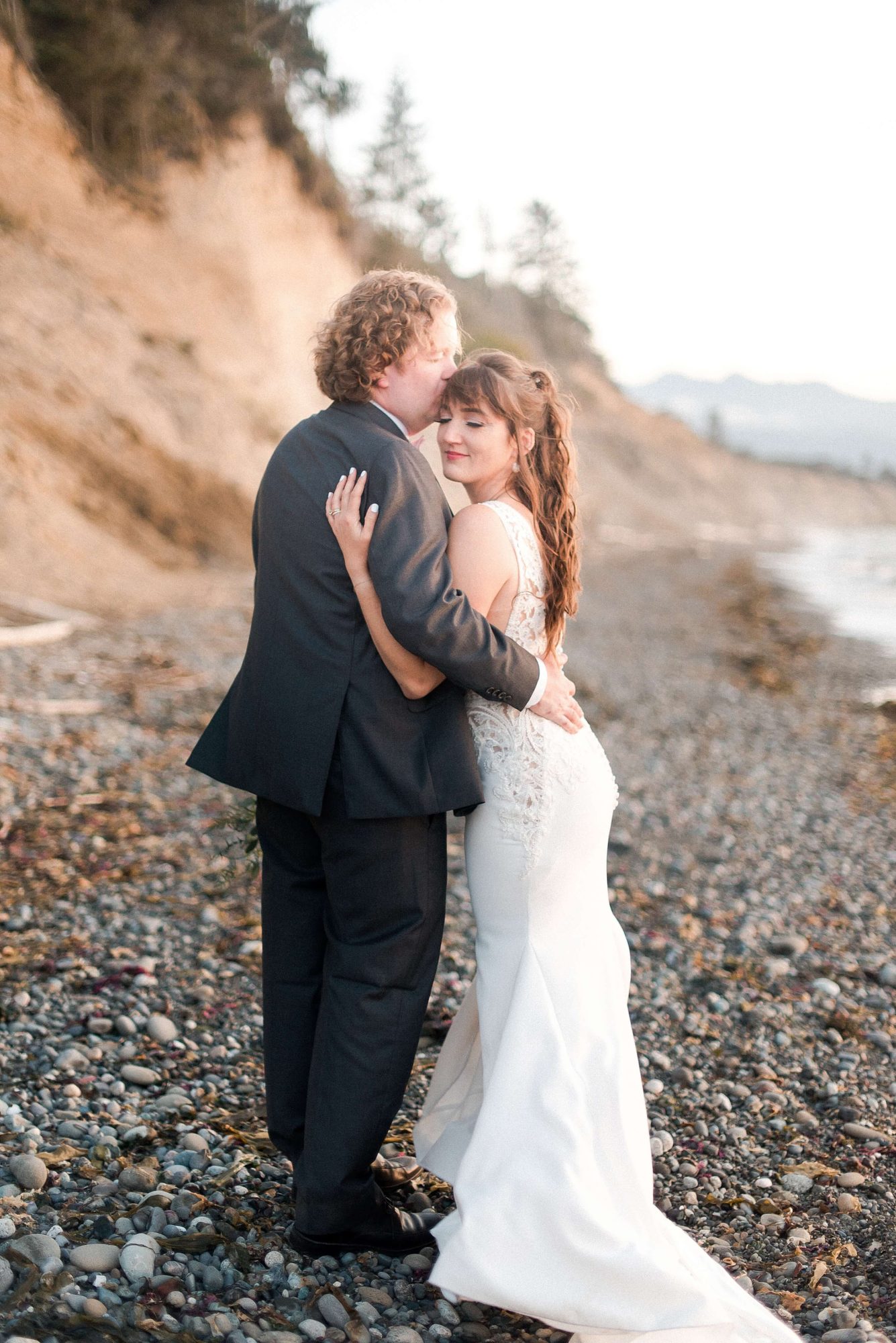 groom kissing his bride on the head on the beach at their Whidbey Island Wedding