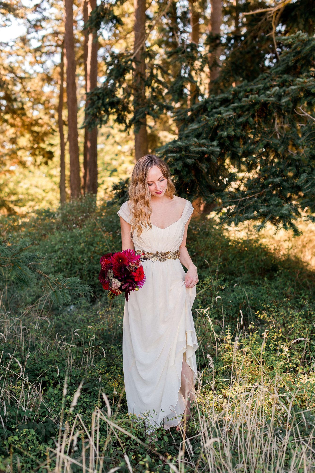 bride holding her dress as she walks through the forest at their Whidbey Island Wedding