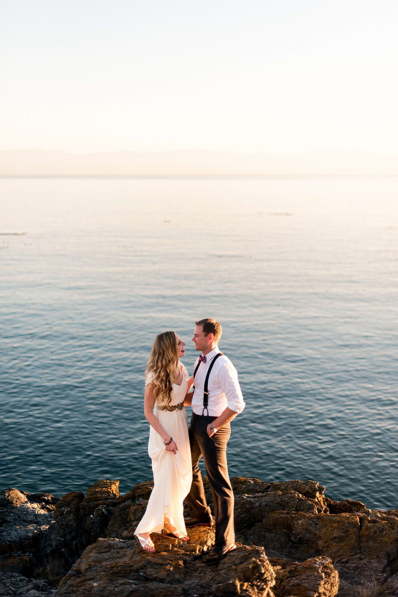 bride and groom standing on a rock near the water at their Whidbey Island Wedding
