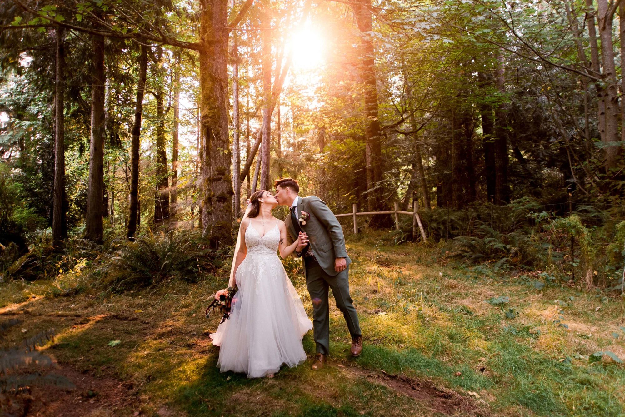 bride and groom kiss under the setting sun through forest trees at The Lodge at St. Edwards